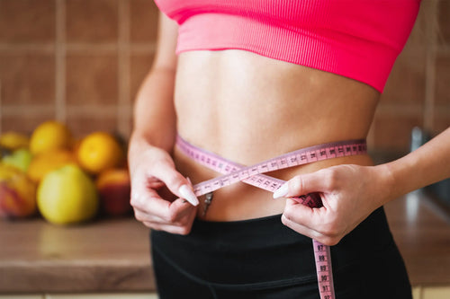 Woman in athletic clothes wrapping pink measuring tape around waist